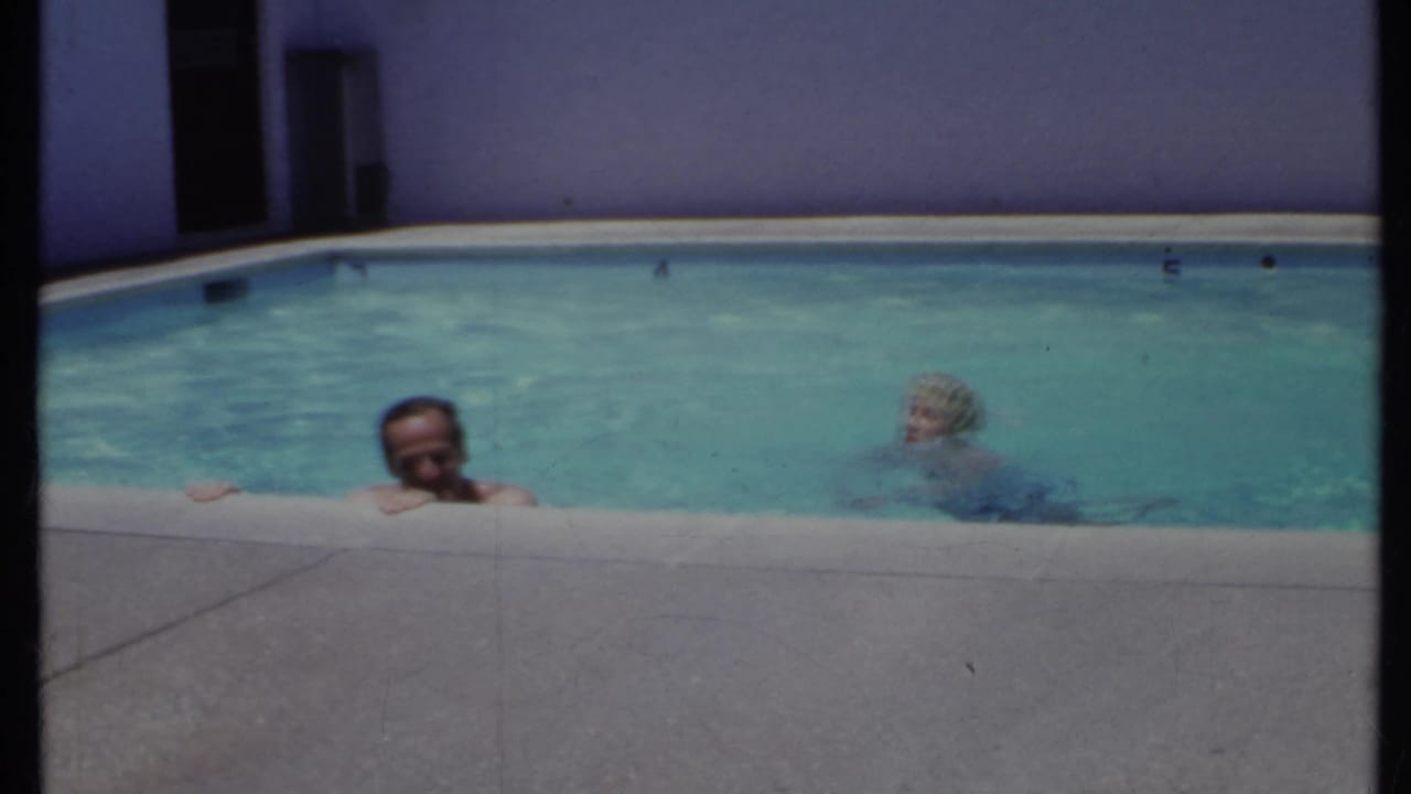 Two adults in a backyard swimming pool beside a concrete pool edge.