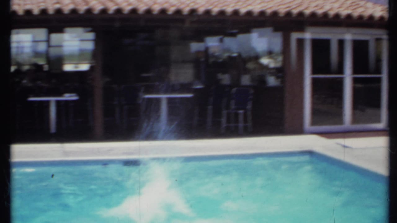Backyard swimming pool in front of a house with tiled roof and shaded patio doors.