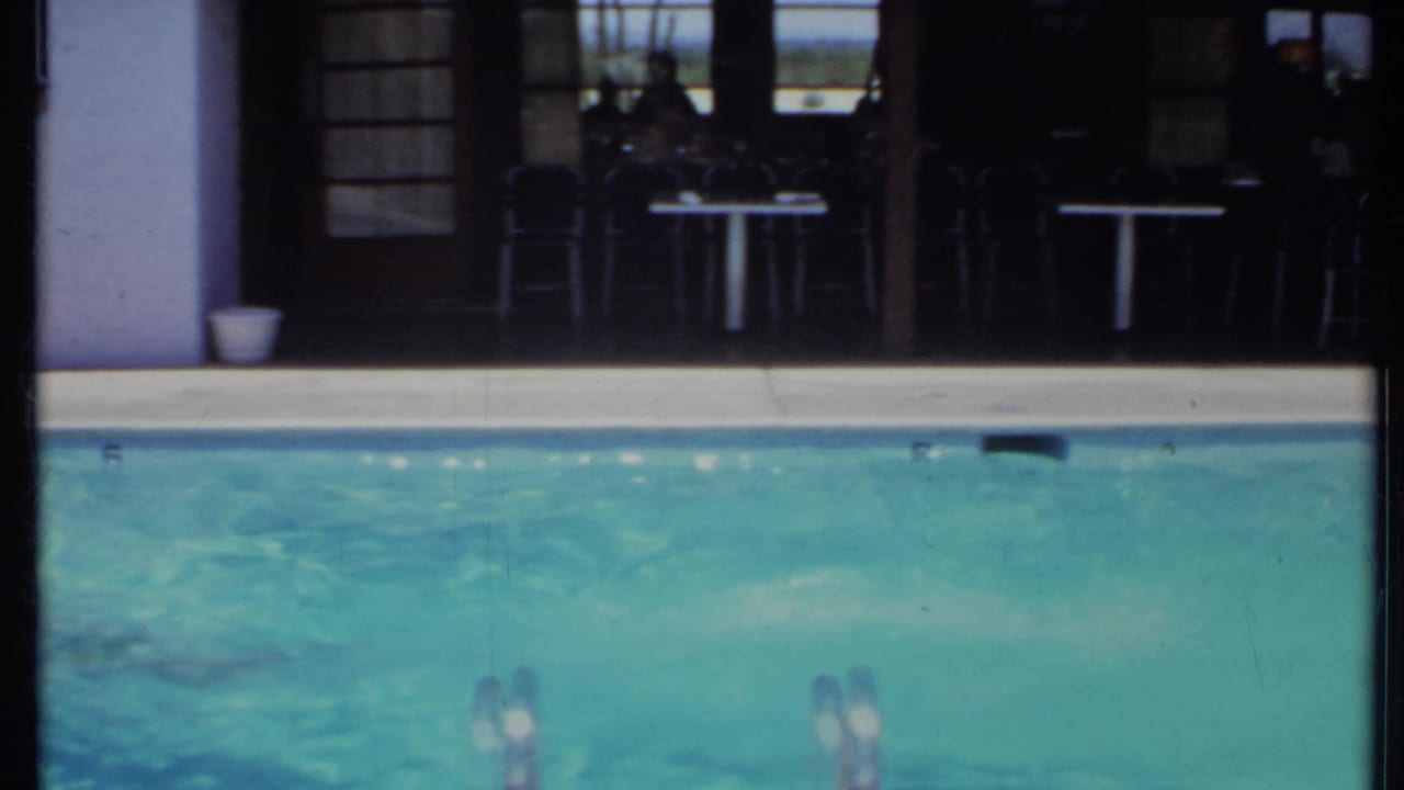 Pool surface with swimmers partly visible near a house patio and glass doors.