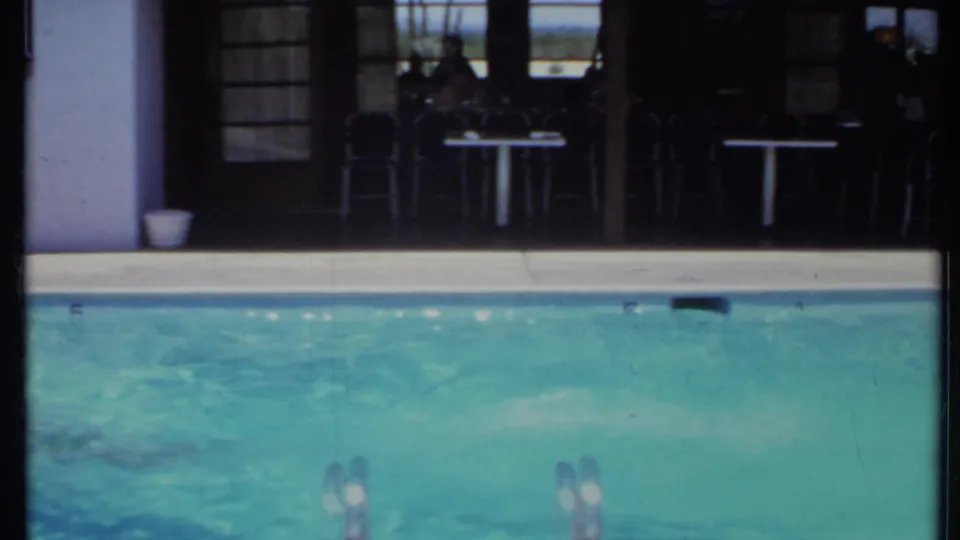 1971 California pool scene with swimmers partly visible in turquoise water beside shaded patio doors and outdoor furniture.