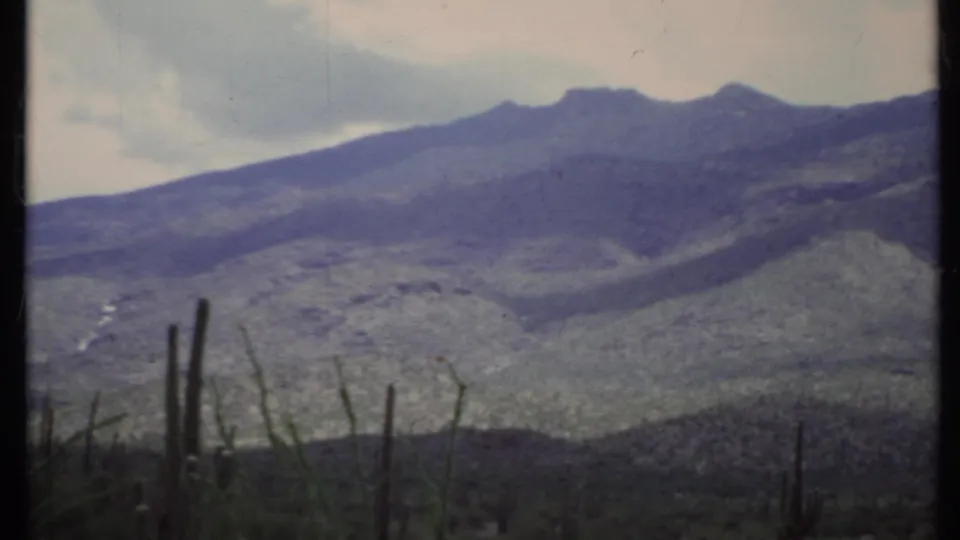 8mm frame showing mountain slopes and possible haze or cloud cover above sparse desert cactus in California.