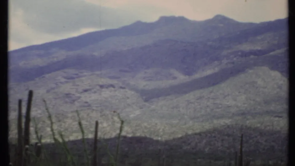 1971 California desert mountain view on 8mm film, with cactus-like stems, cloudy sky, and faded home-movie color.