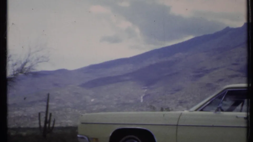 The car is partly out of frame as cactus forms and a broad mountain slope dominate the 1971 California desert view.
