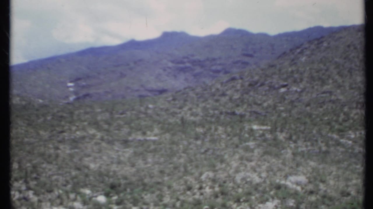 Arid scrub valley with rocky slopes and distant mountains.