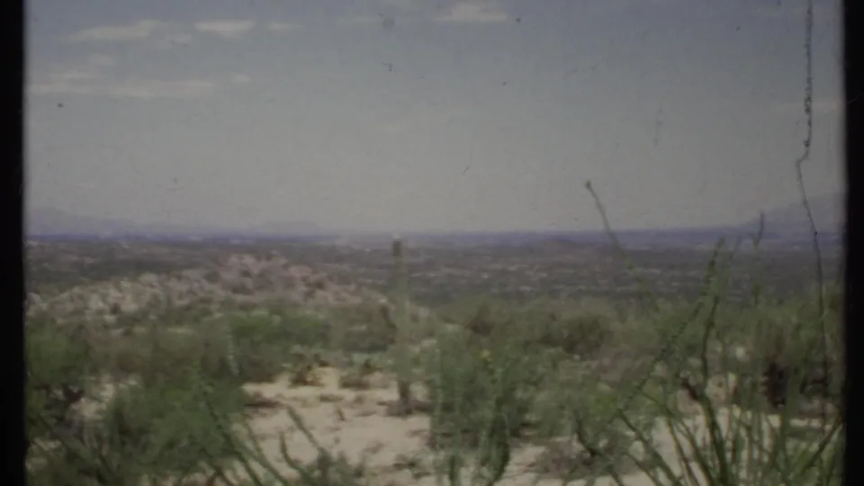 A 1971 California desert panorama shows scrubby plants, pale soil, low hills, and distant mountains in soft 8mm color.