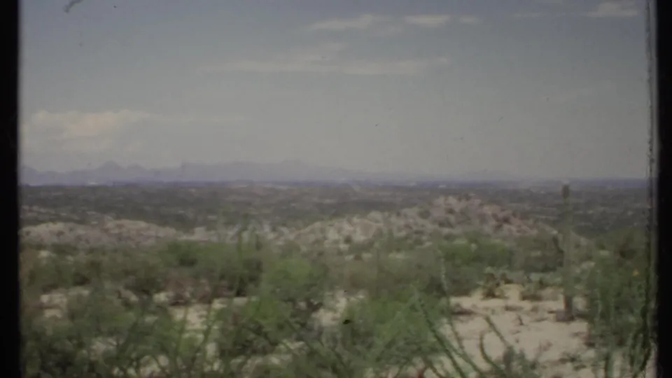 The final 1971 California desert frame shows foreground shrubs, pale sandy terrain, low hills, and hazy mountains under bright daylight.