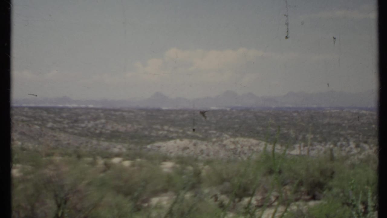 Wide arid landscape with scrub, distant hills, and hazy mountains.