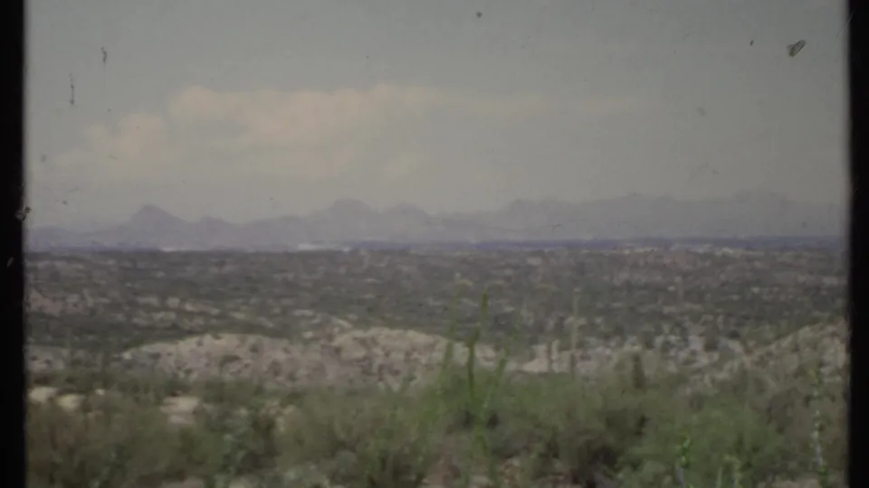 Home-movie view of California desert terrain in 1971, with brush in the foreground and layered mountains beneath a washed sky.