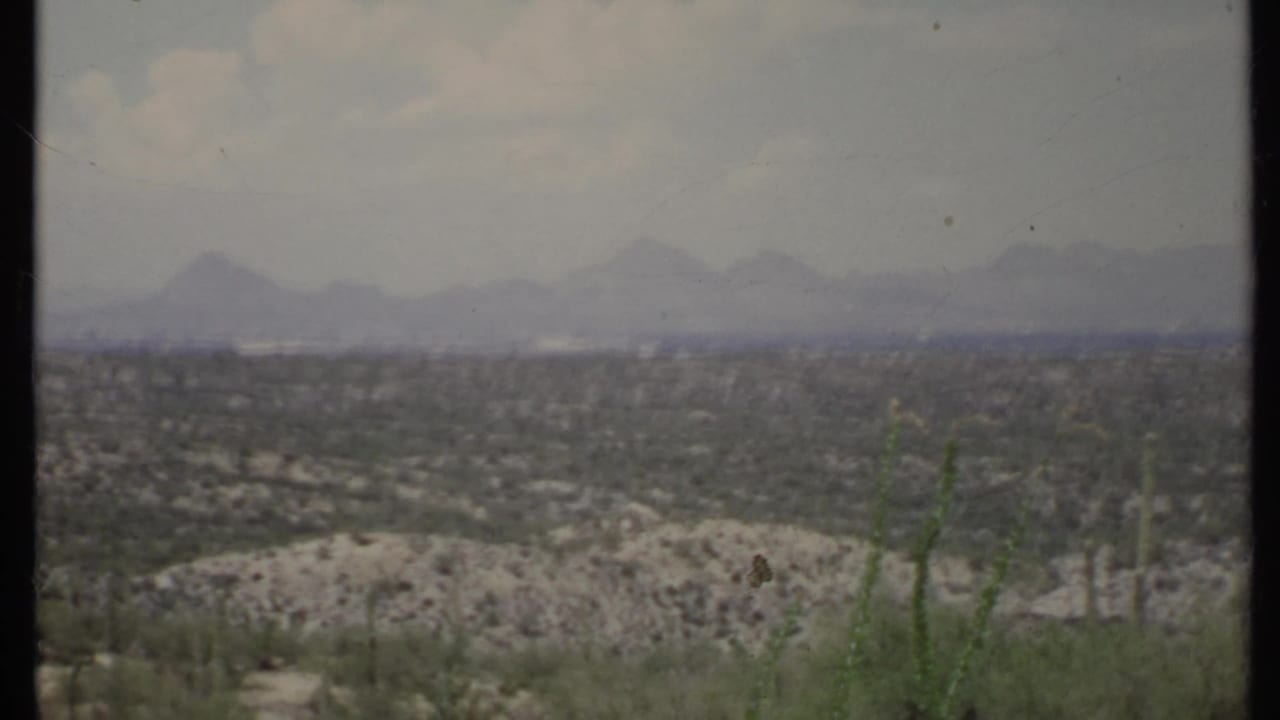 Hazy desert valley with distant mountains and sparse scrub in the foreground.