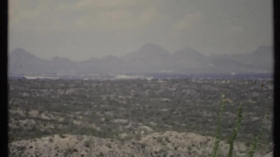 1971 8mm California landscape frame showing distant mountains beyond a broad arid valley and scrub-covered foreground.