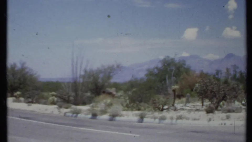 Roadside desert landscape in California, 1971, with scrub plants, distant mountains, and a bright clouded sky.