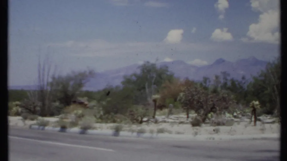 1971 8mm roadside view of desert vegetation and distant mountains, seen from a moving vehicle in California.