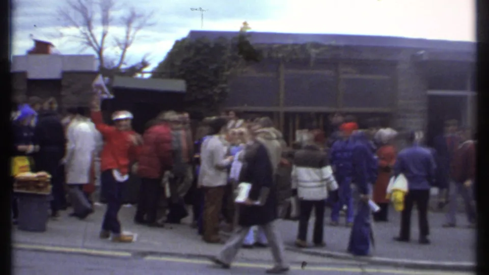 The 1979 Ithaca crowd continues outside the entrance, with people standing in groups and moving along the curb.