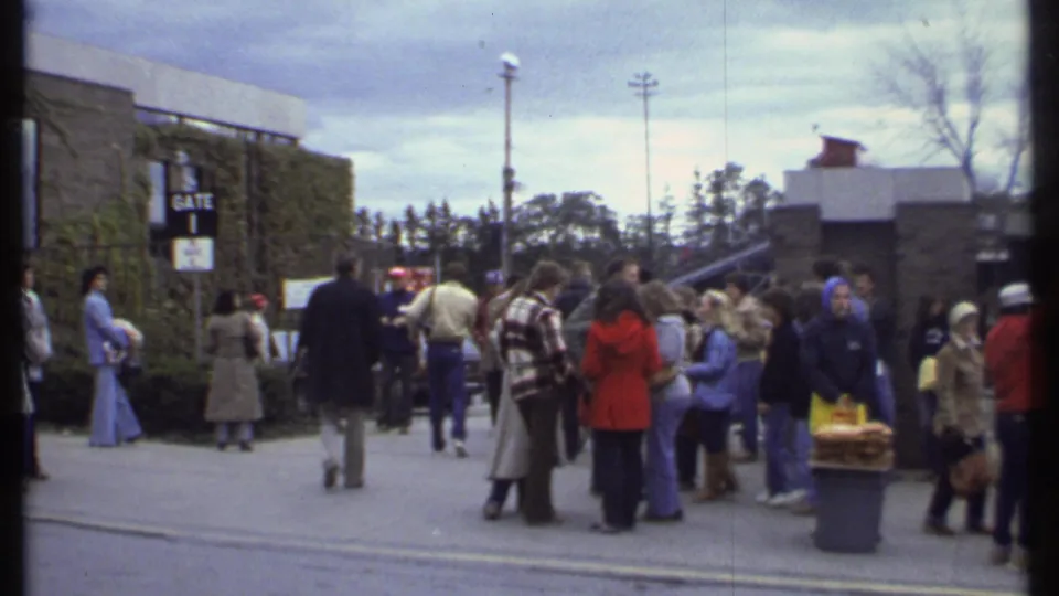 1979 Ithaca crowd scene with a visible Gate 1 sign, adults in coats, trees, and a paved approach to a building entrance.