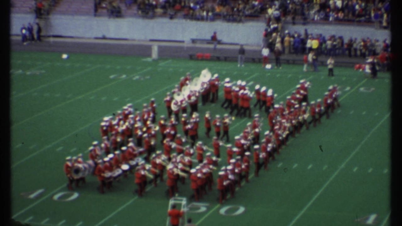Marching band in red uniforms forms a large shape on a football field.