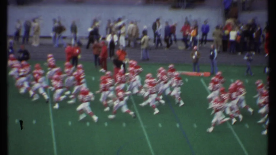 Closer home-movie frame from the 1979 Ithaca football game showing motion-blurred players and spectators along the sideline.