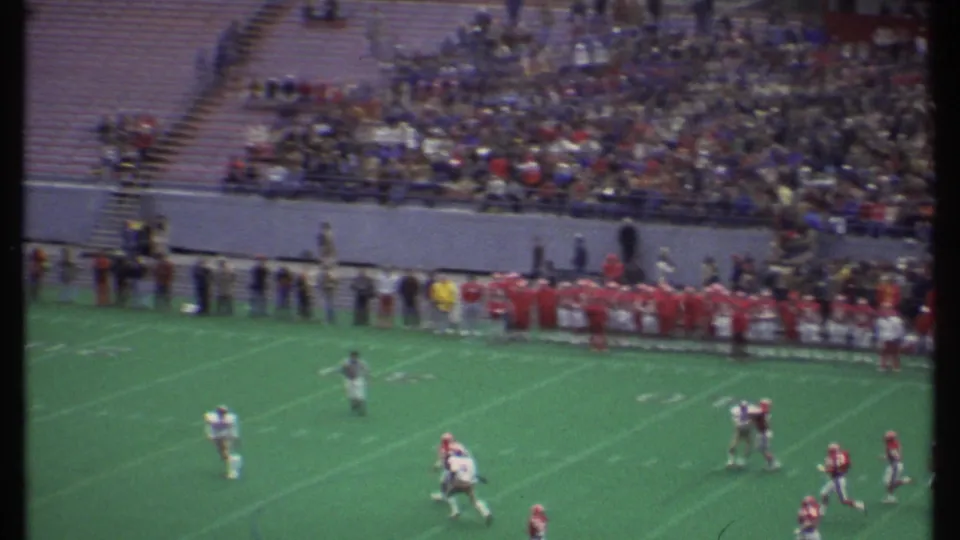The home-movie view catches a football play near the sideline, with teams and spectators visible in the stadium.