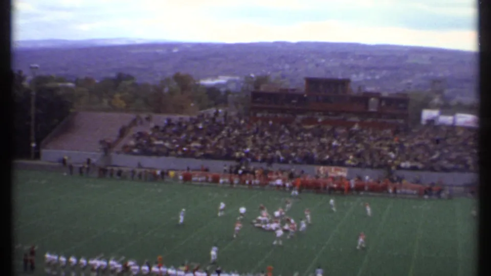 Home-movie stadium angle from Ithaca in 1979, showing a football play near midfield with spectators across the stands.