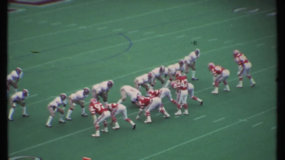 1979 Ithaca football action with red and white uniformed players lined up before the snap on a green field.
