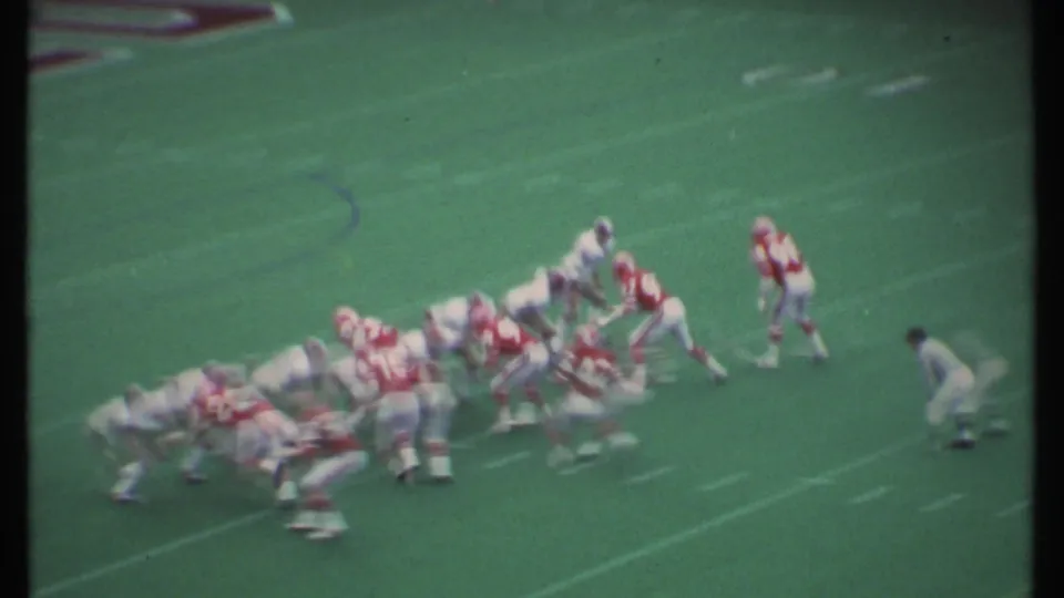 1979 Ithaca, New York football players in red and white uniforms set for a play on a green artificial turf field.