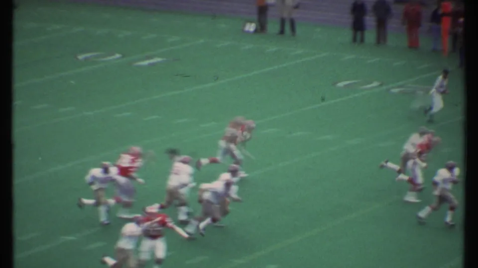 A football runner advances through pursuing players in vintage 8mm footage from Ithaca, New York in 1979.