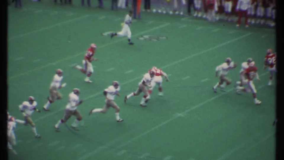 Players run downfield on a marked green field during a 1979 Ithaca, New York football game filmed from the stands.