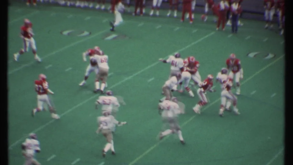 American football action in Ithaca, New York, with red and white teams blocking and pursuing the ball carrier.