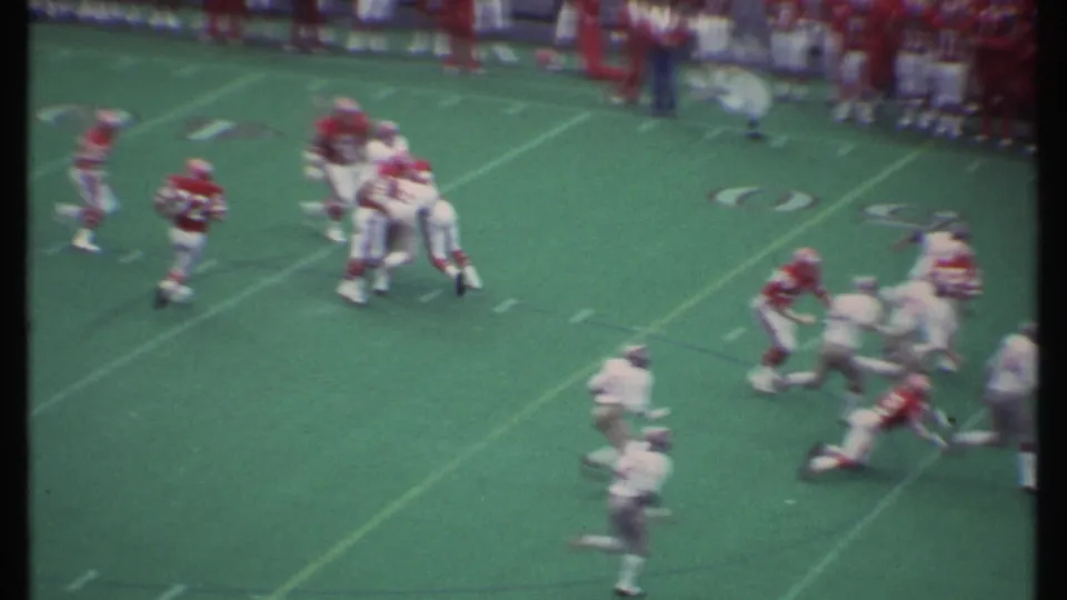 Close handheld 8mm view of football players in red and white uniforms colliding during a tackle in Ithaca.