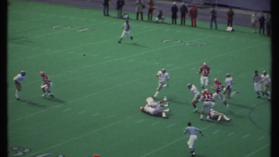 Closer 1979 Ithaca football moment showing a tackle or block, with several players on the ground and others nearby.