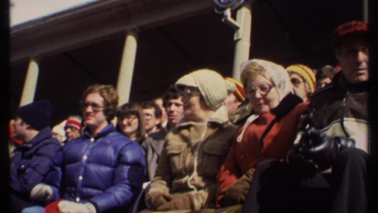 Bundled spectators sit in stadium seating, including people in knit hats and winter coats.