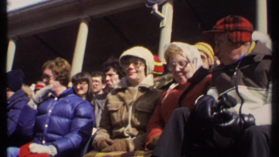 Close spectator view at a 1979 Ithaca football game, with adults in heavy coats and knit hats seated in bright sun.