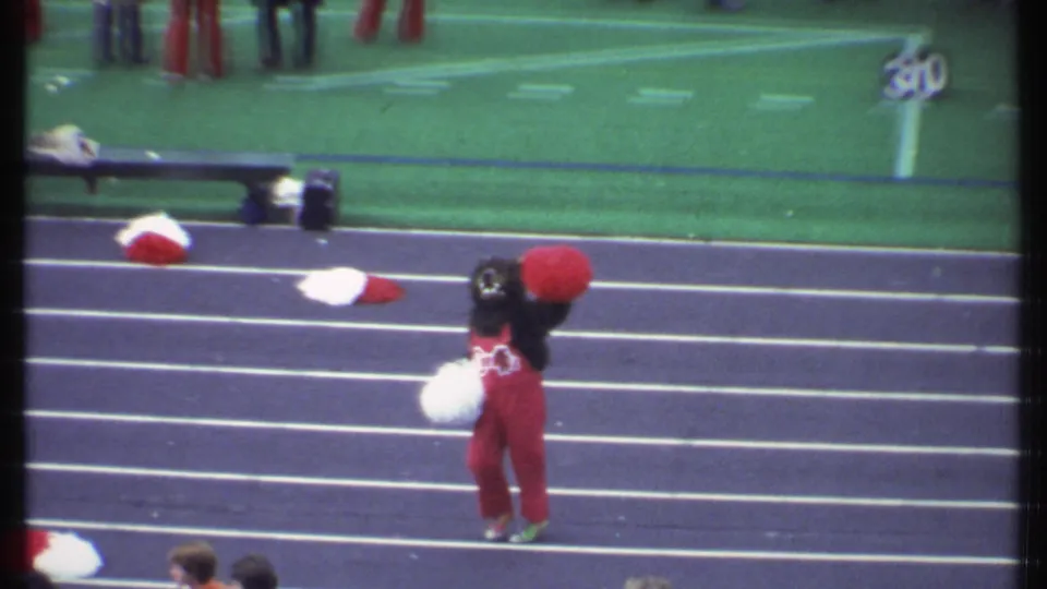 A red-and-white college mascot performs on the track beside the football field during the 1979 Ithaca game footage.