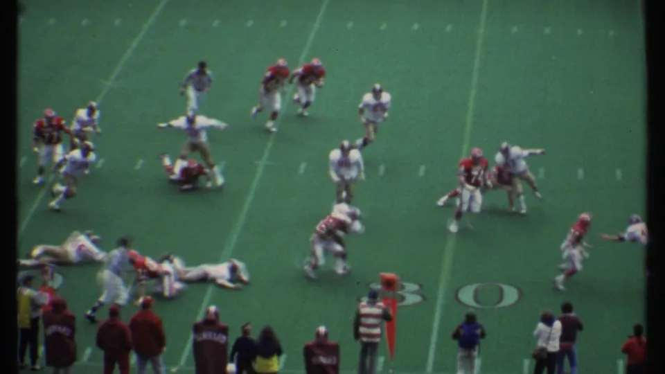 The game continues in Ithaca, New York, with red and white football players scattered after a tackle near visible yard markings.