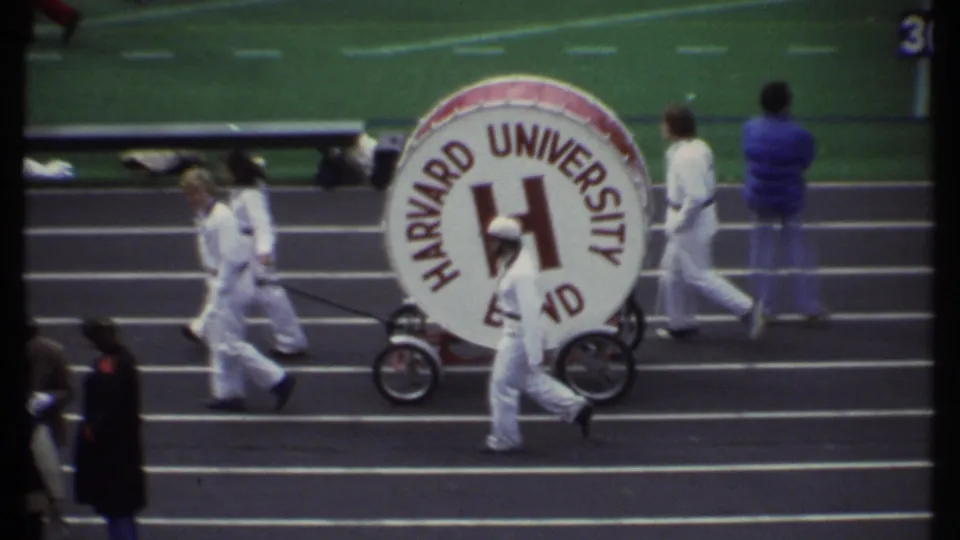 The 1979 Ithaca football scene shows the Harvard University Band bass drum being wheeled past sideline personnel.