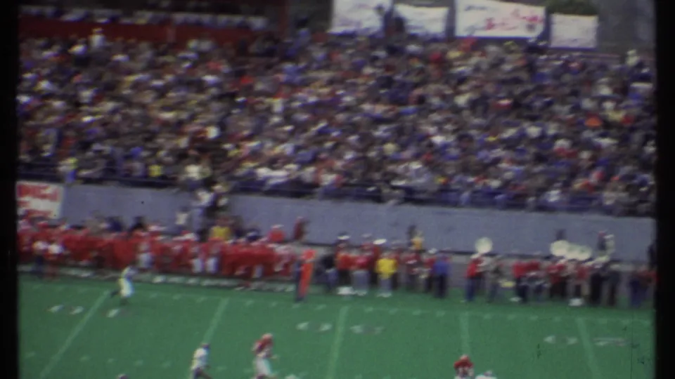 A soft 8mm view shows the stadium crowd, football sideline, and band activity during a 1979 college game in Ithaca.