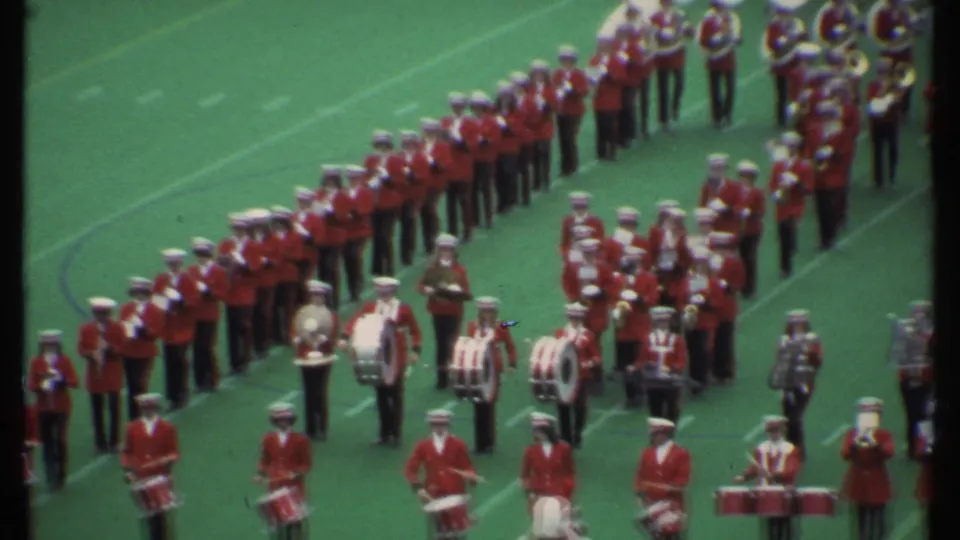 Closer 1979 Ithaca home-movie view of red-and-white marching band members, including drummers, arranged on a football field.