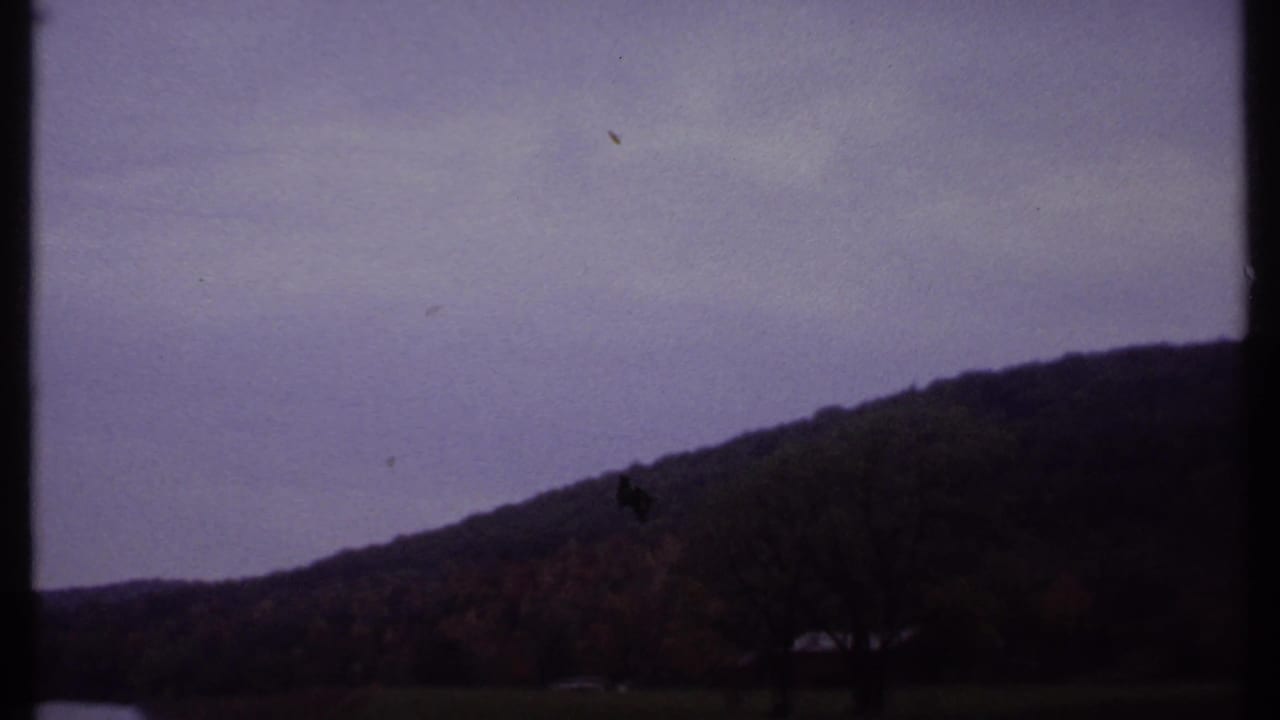 Overcast sky above a dark wooded hillside with water or open foreground below.