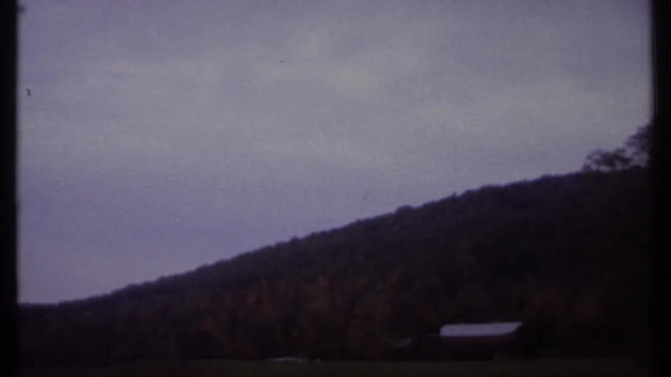 1979 8mm view near Ithaca showing a plowed field, autumn hillside, overcast sky, and dark vehicle-window divider.