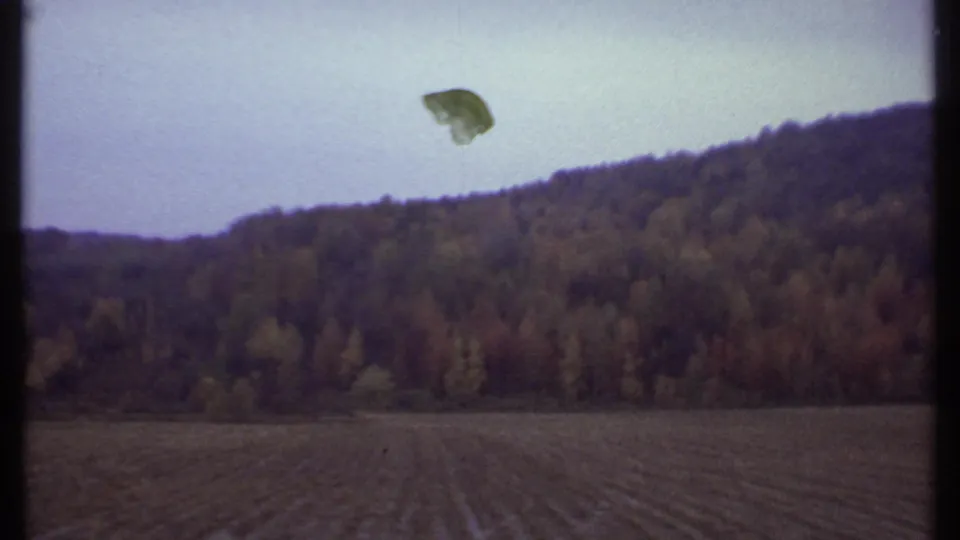 Moving 8mm car-window view near Ithaca, with an autumn hillside, field rows, pale sky, and a small film or window artifact visible above the trees.