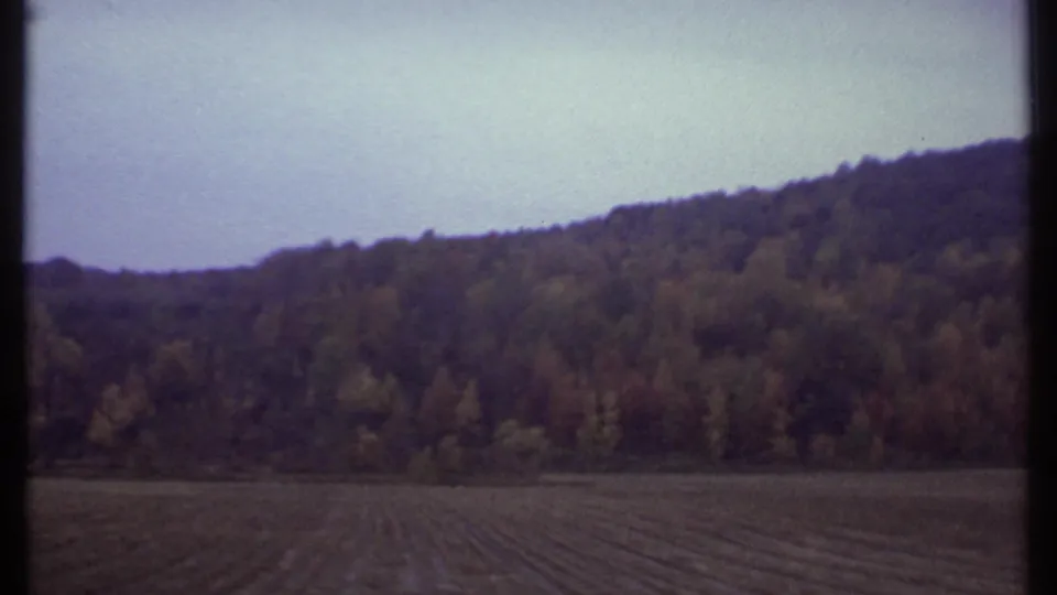 1979 8mm view near Ithaca showing a plowed field and autumn-colored wooded hillside from a moving vehicle.
