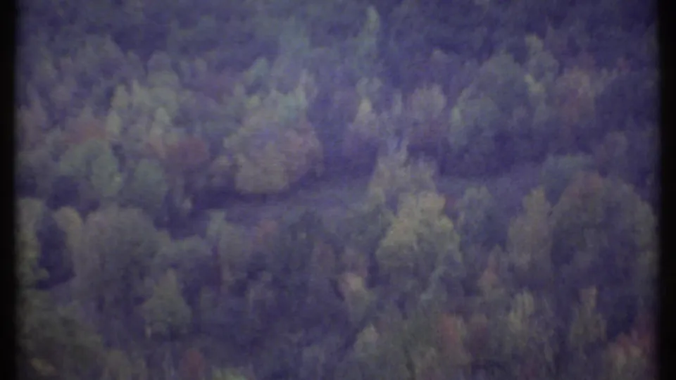 Tree-covered hills near Ithaca appear in faded 8mm color, with the car-window view drifting across the landscape.
