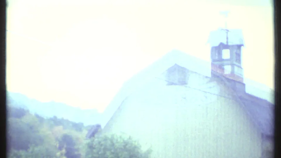 A pale rural barn near Ithaca appears from the moving 1979 8mm viewpoint, topped by a cupola and weather vane.