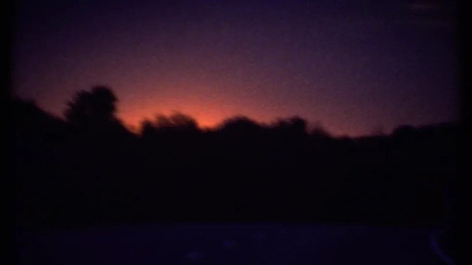 1979 Ithaca frame showing an orange horizon glow and purple sky behind a dark silhouetted treeline.