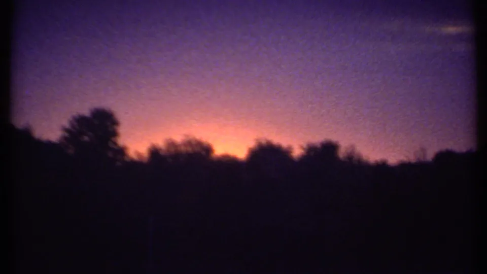 Late-1970s 8mm home-movie frame showing the Ithaca horizon at dusk, with saturated sunset color behind dark trees.