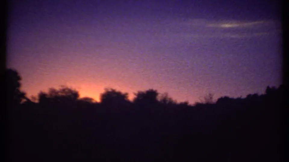 Final 8mm frame of the Ithaca sunset clip, holding on a dark tree line beneath a fading orange and purple-blue dusk sky.