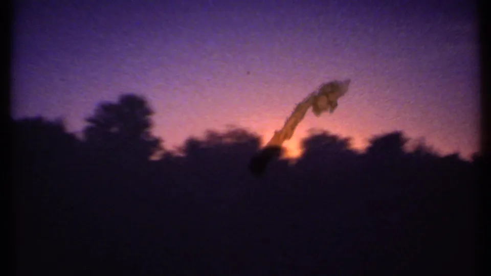 8mm frame from Ithaca, New York, with silhouetted trees and a warm orange sunset beneath a purple sky.