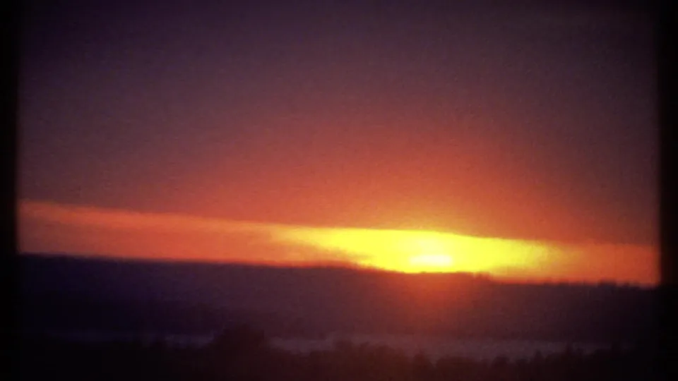 8mm Ithaca sunset frame showing yellow light over a dark ridge, with possible water or haze reflecting the glow below.