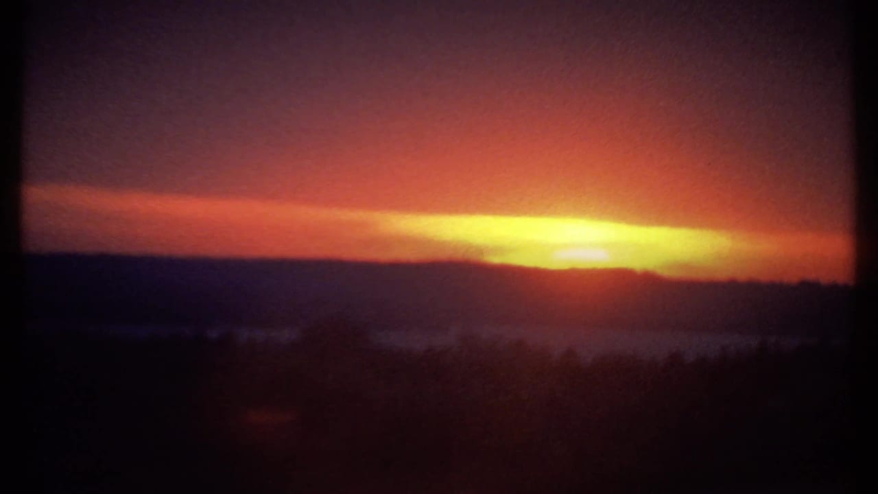 Bright sunset over dark hills with orange clouds and purple sky.