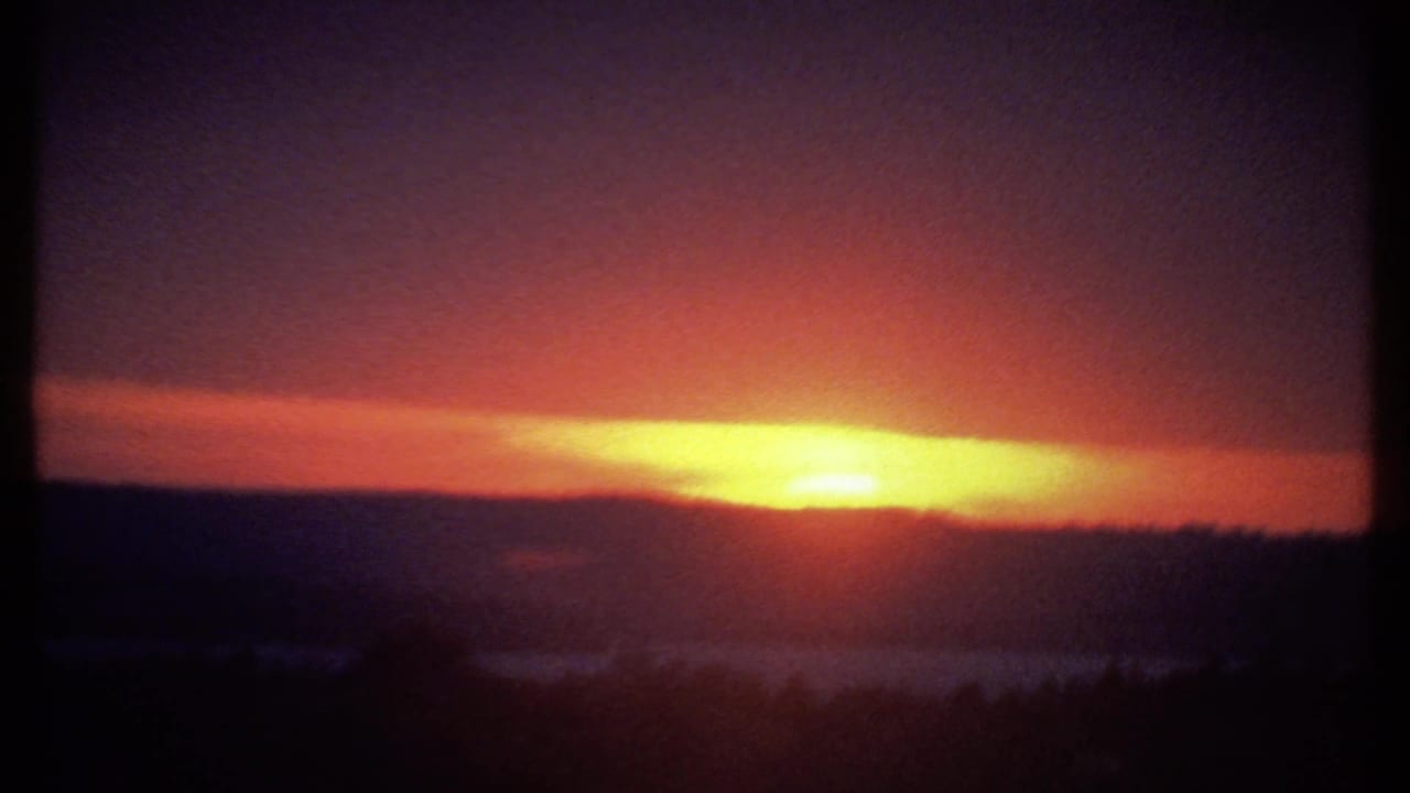 Passenger-window view of the 1979 Ithaca sunset, with the sun flaring near the horizon and dark vertical frame shadows at the sides.