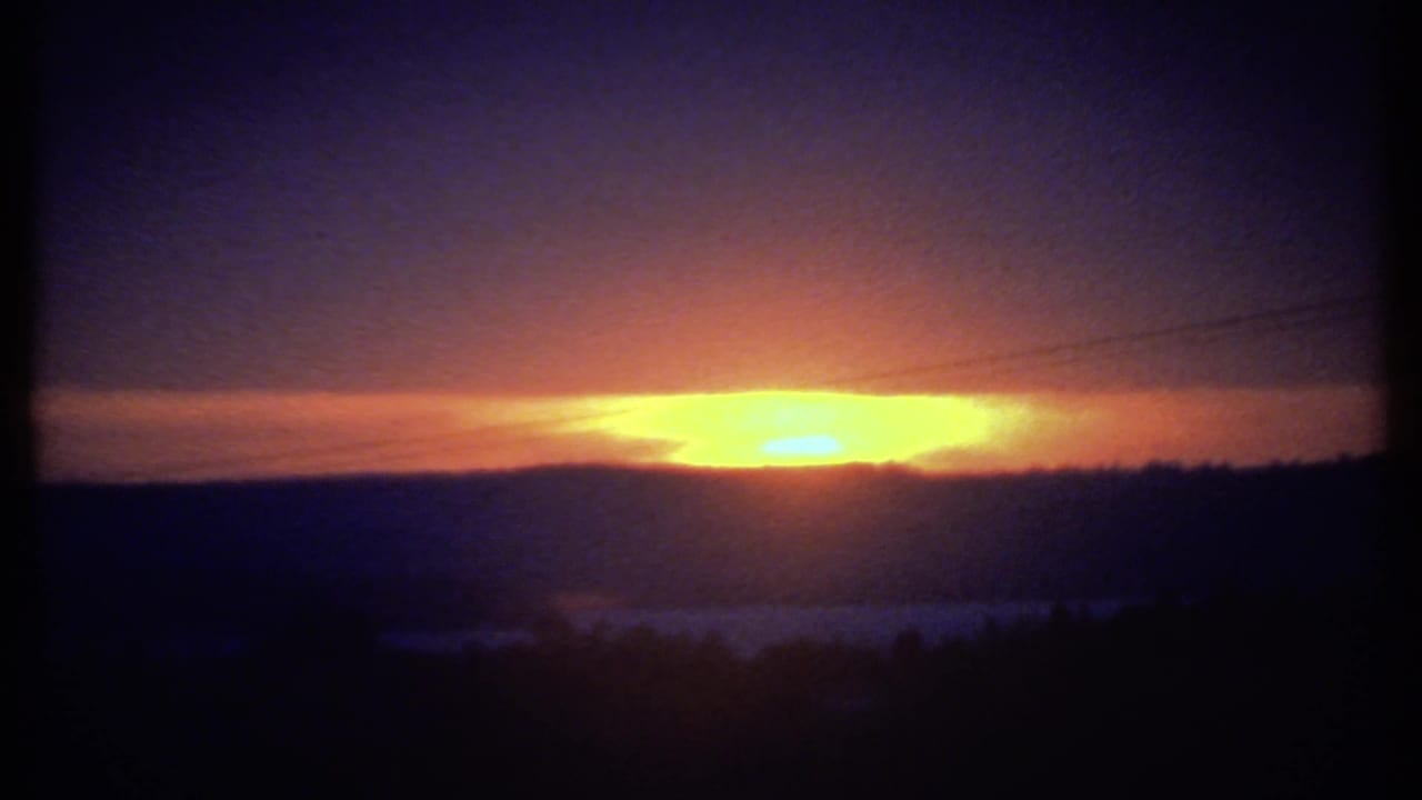 Yellow-orange sunset over dark hills with silhouetted trees and utility wires.